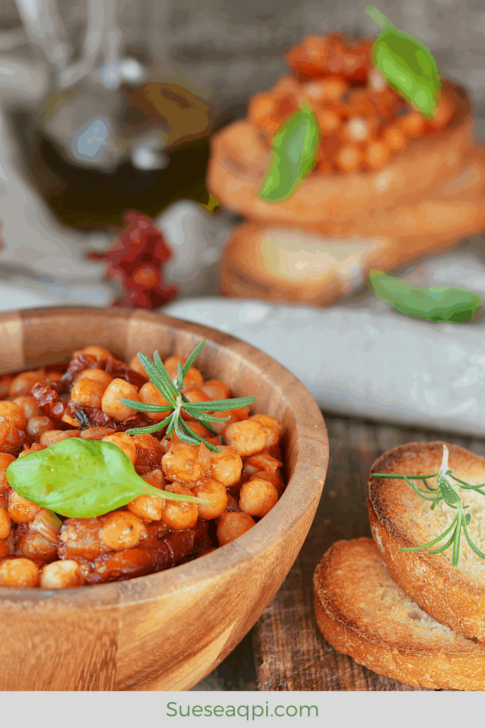 Chickpea stew in a wooden bowl basil and rosemary garnish and 2 slices of toasted Italian bread on the side