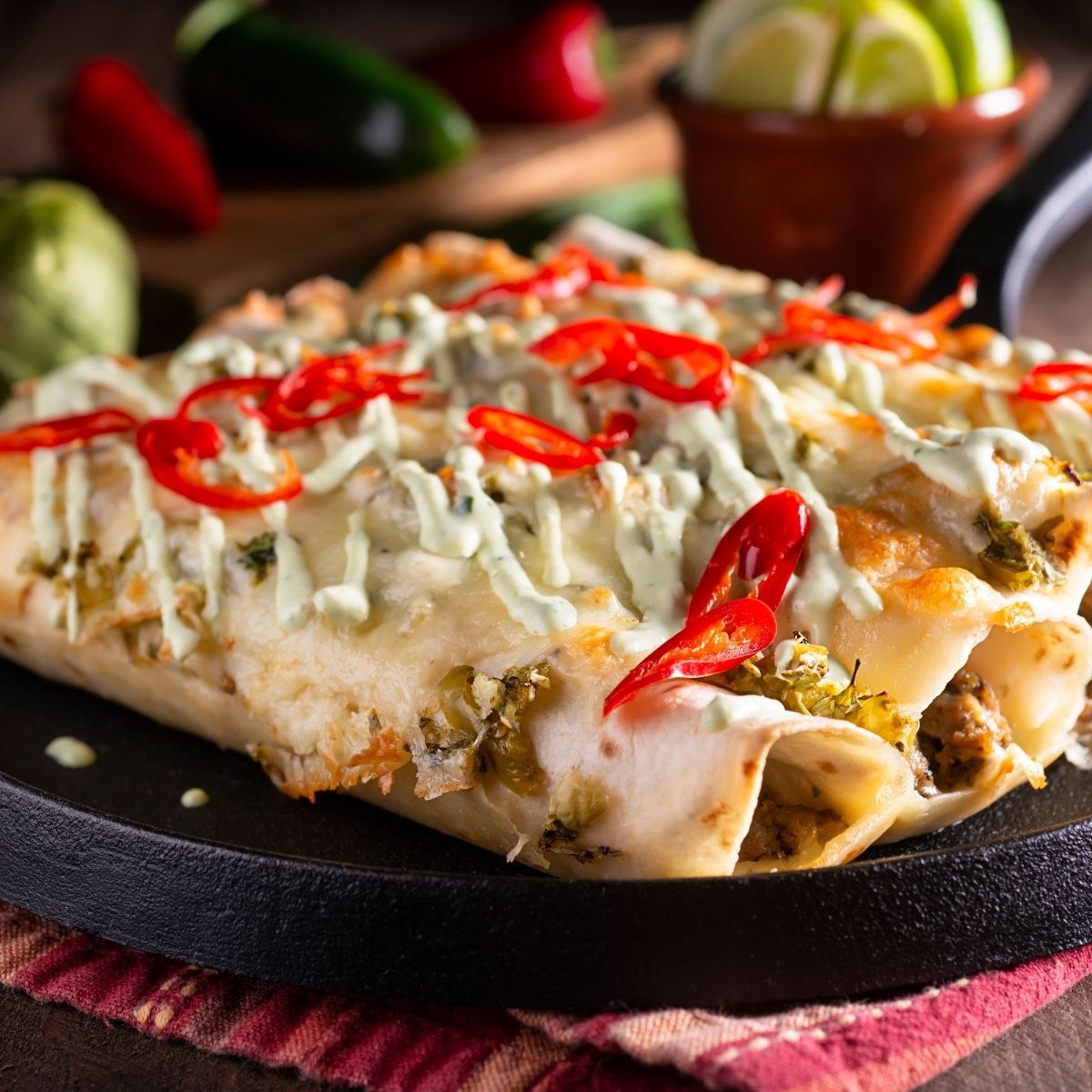 Four Chicken enchiladas in a black baking dish with diced red peppers on top