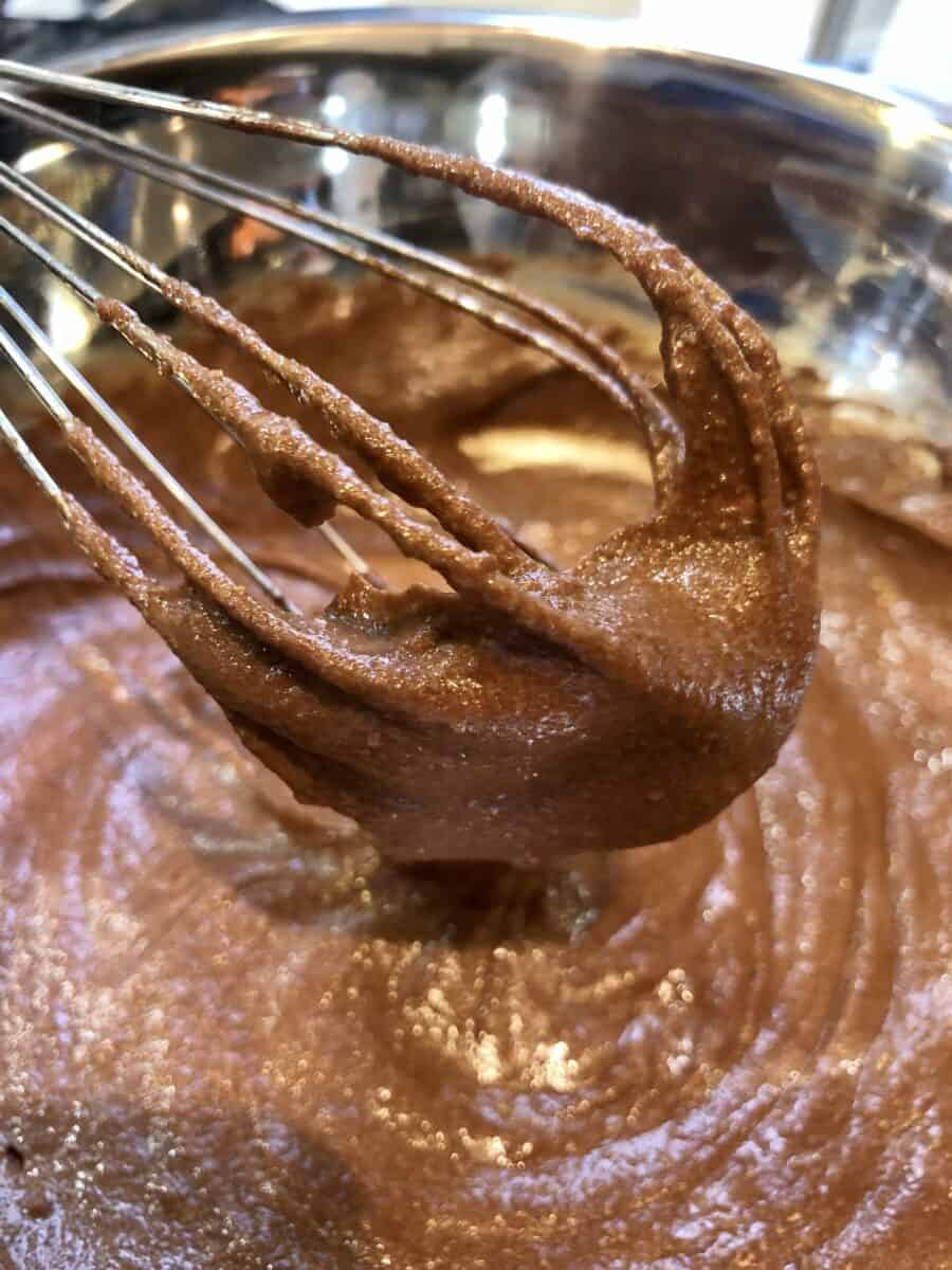 Chocolate Cake Batter on a whisk in a stainless steel bowl