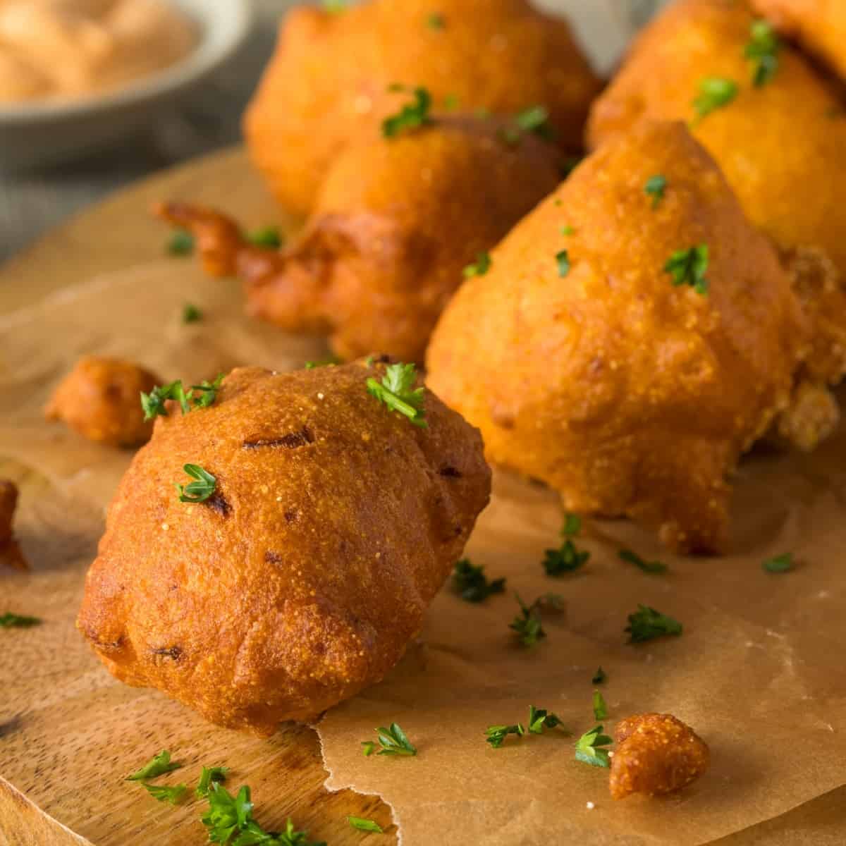 Air Fryer Hush Puppies on a wooden cutting board with parchment paper and chopped parsley