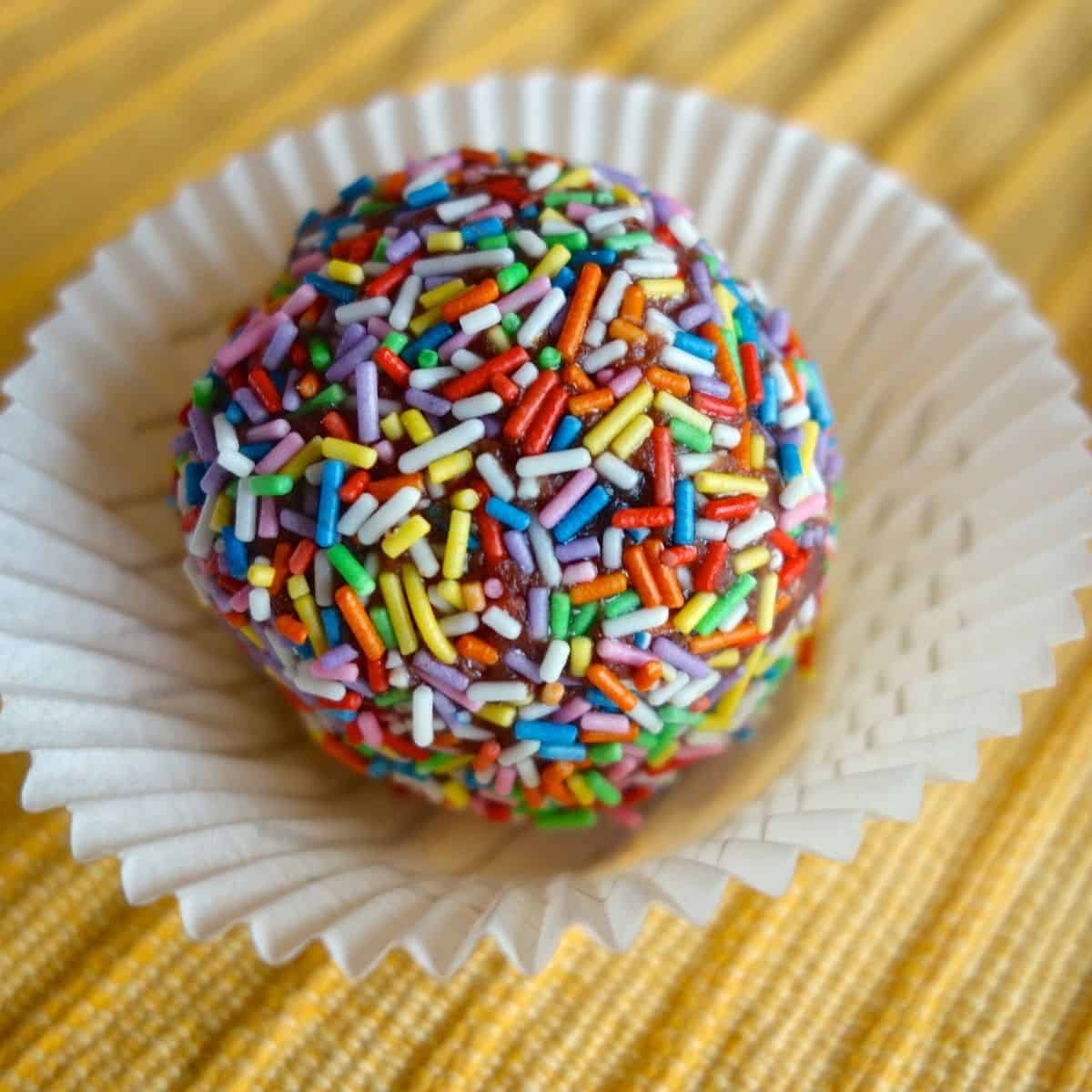 Rainbow Sprinkle Protein Ball in a white paper cupcake holder on a yellow place mat