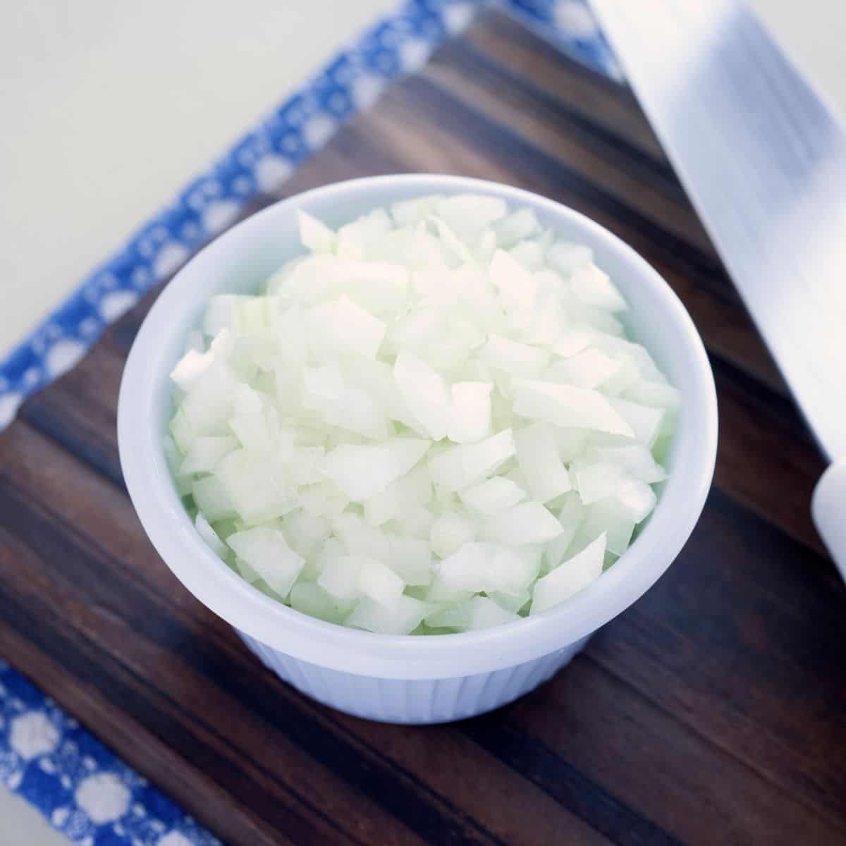 diced onions in a small white bowl on a wooden table