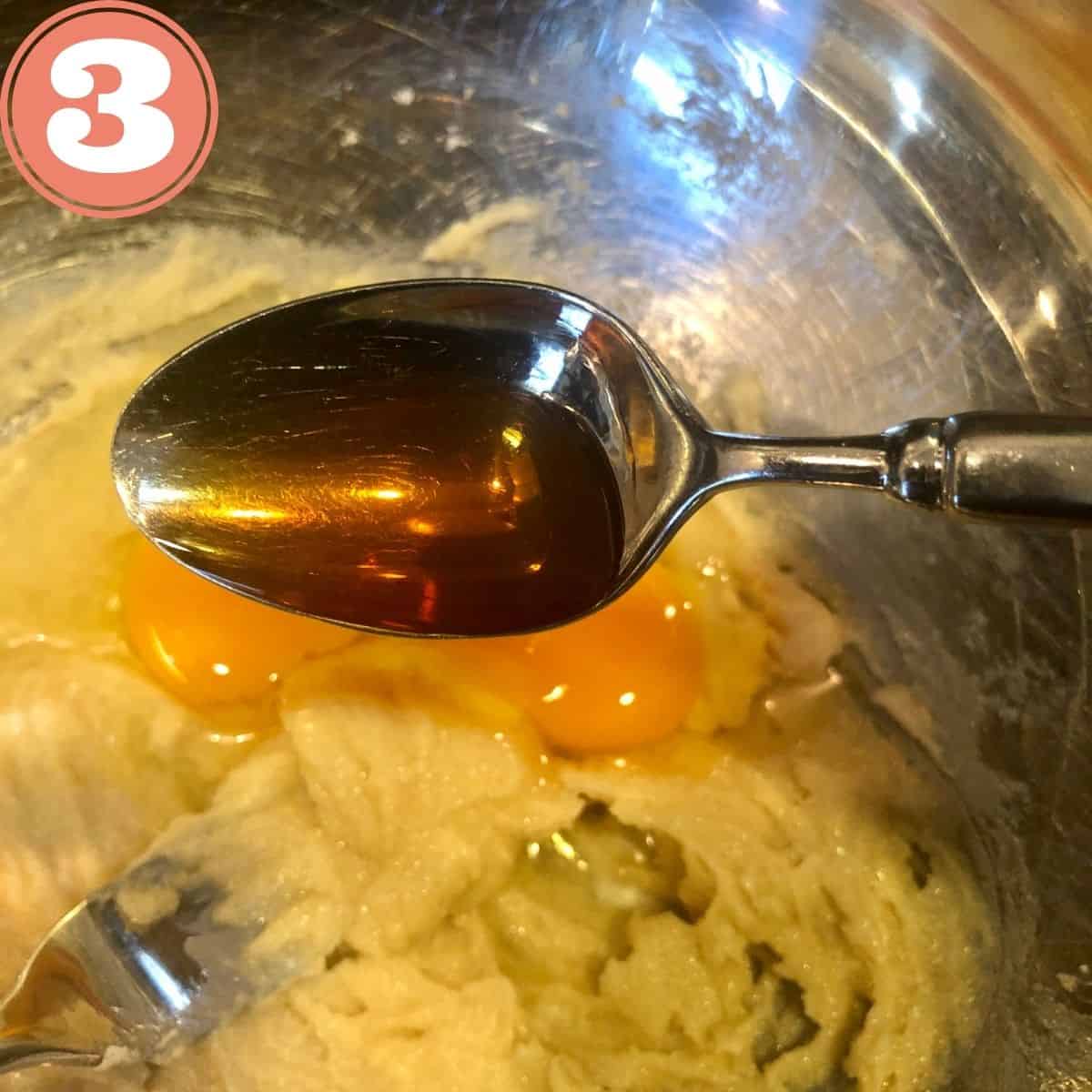 A spoonful of Vanilla extract being poured into the egg and cookie batter in mixing bowl