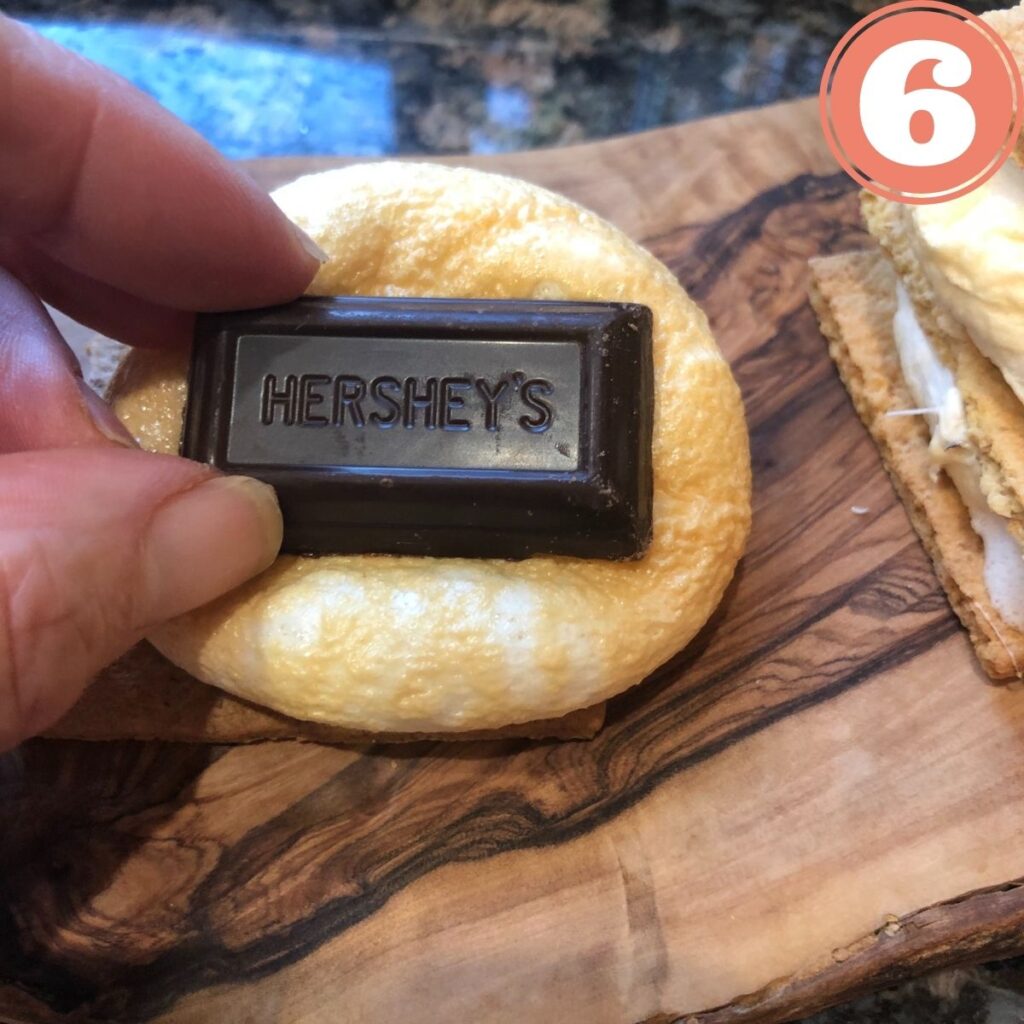 Hershey's miniature chocolate bar on top of a toasted marshmallow on a graham cracker sitting on a wooden cutting board