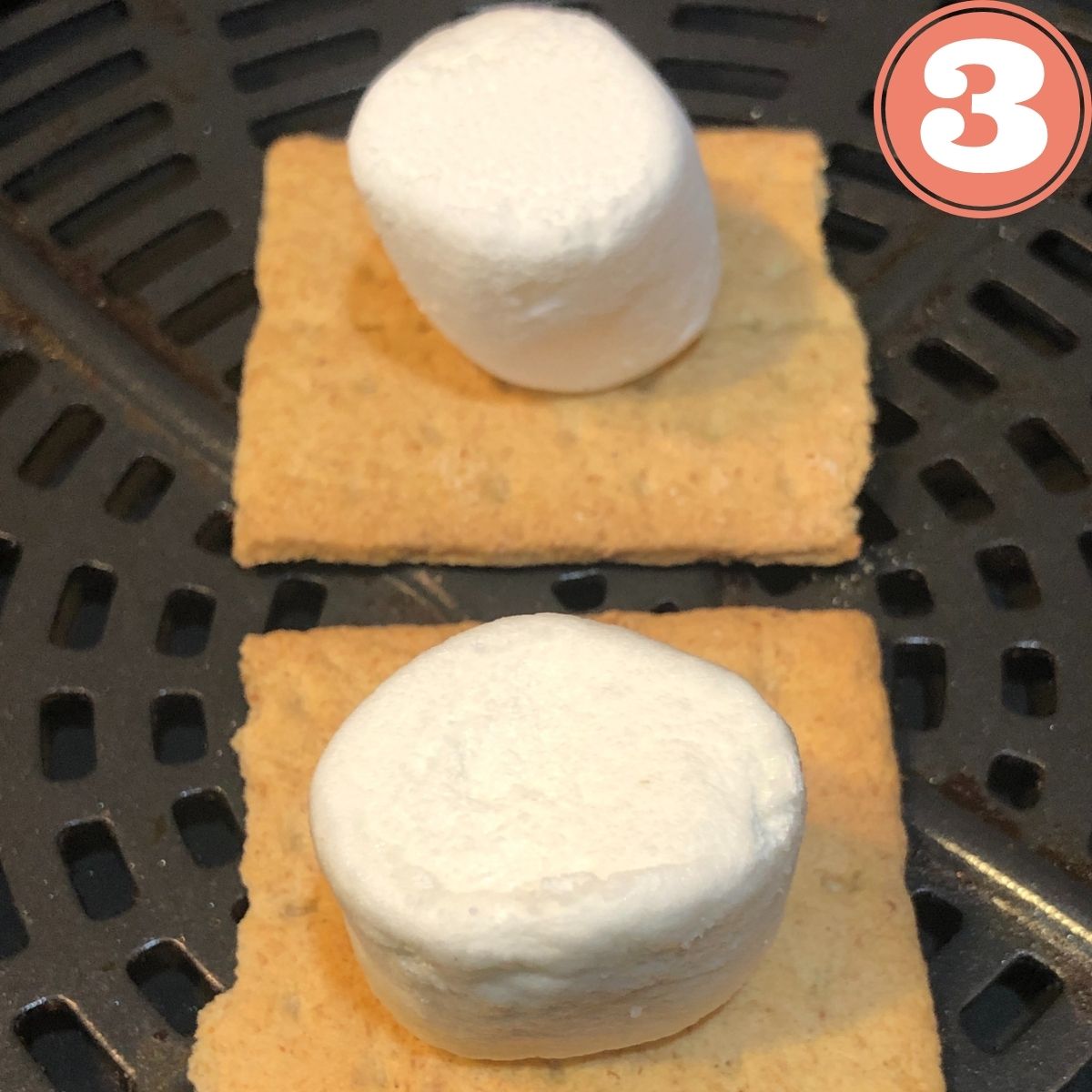 Two graham crackers with a marshmallow on top sitting in an air fryer basket