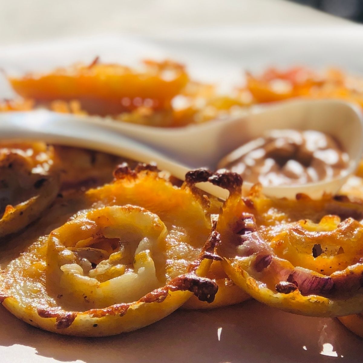 Keto Onions Rings with Cheese stacked on a sheet of parchment paper with spicy keto sauce in a white spoon