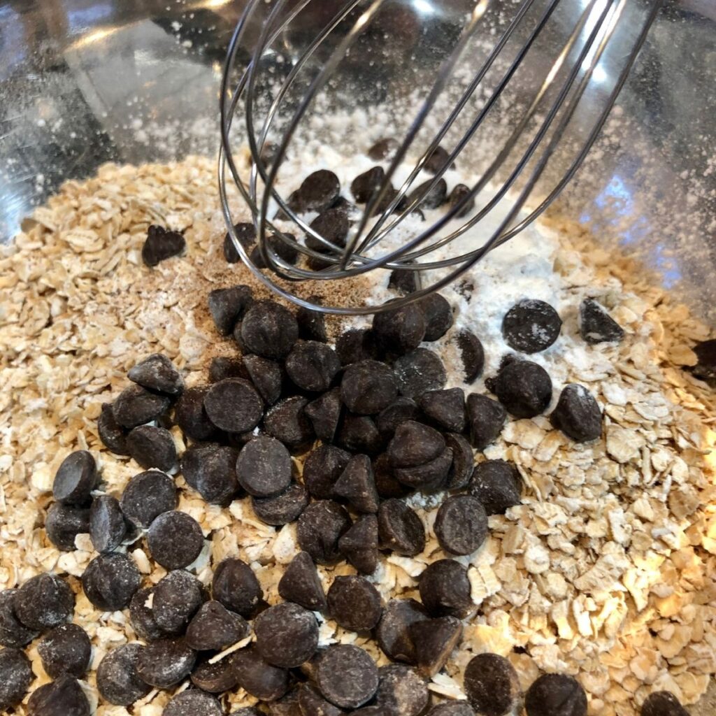 a bowl of oatmeal and chocolate chips with a whisk