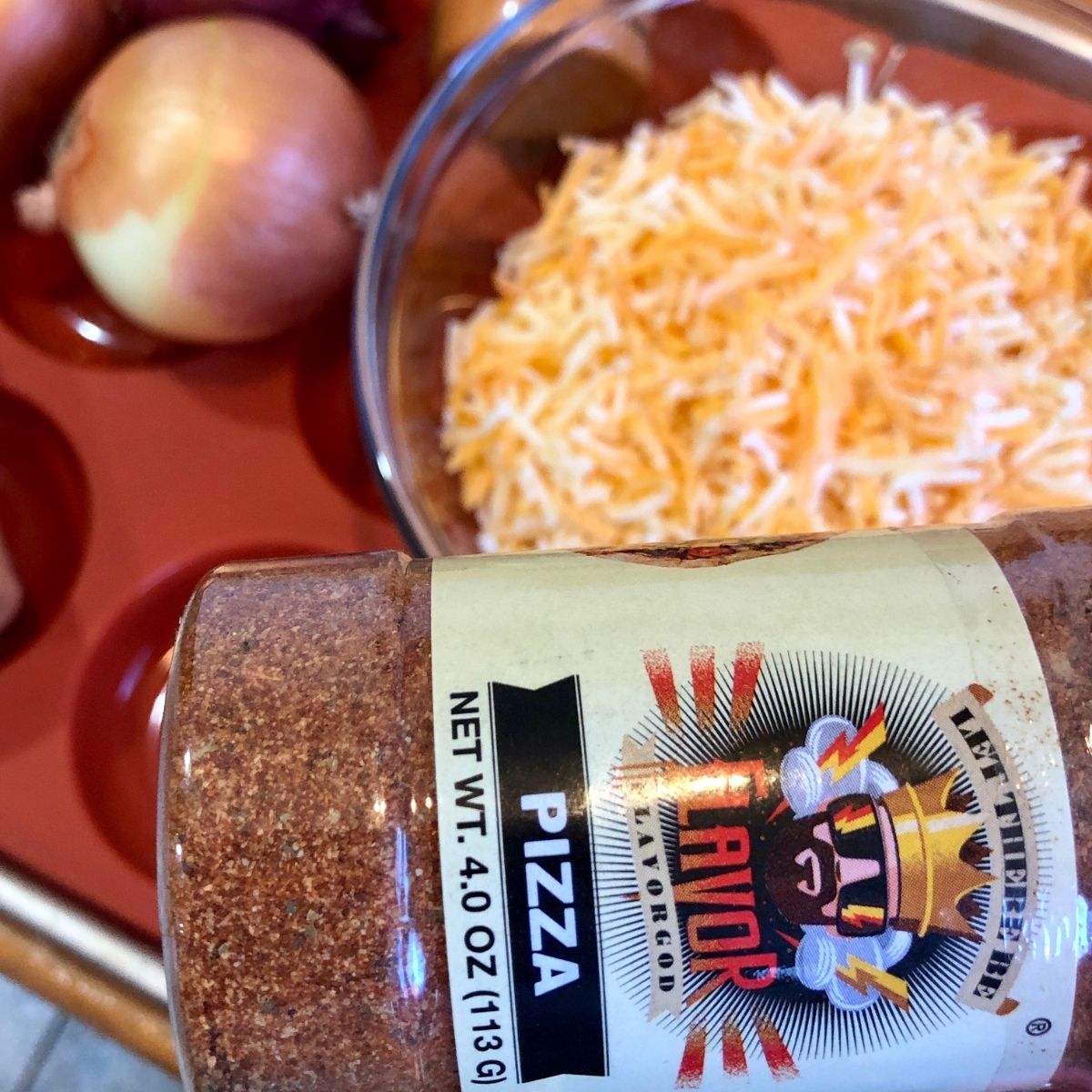 Flavor Goods Pizza Seasoning with a bowl of shredded cheese and an onion in a donut pan