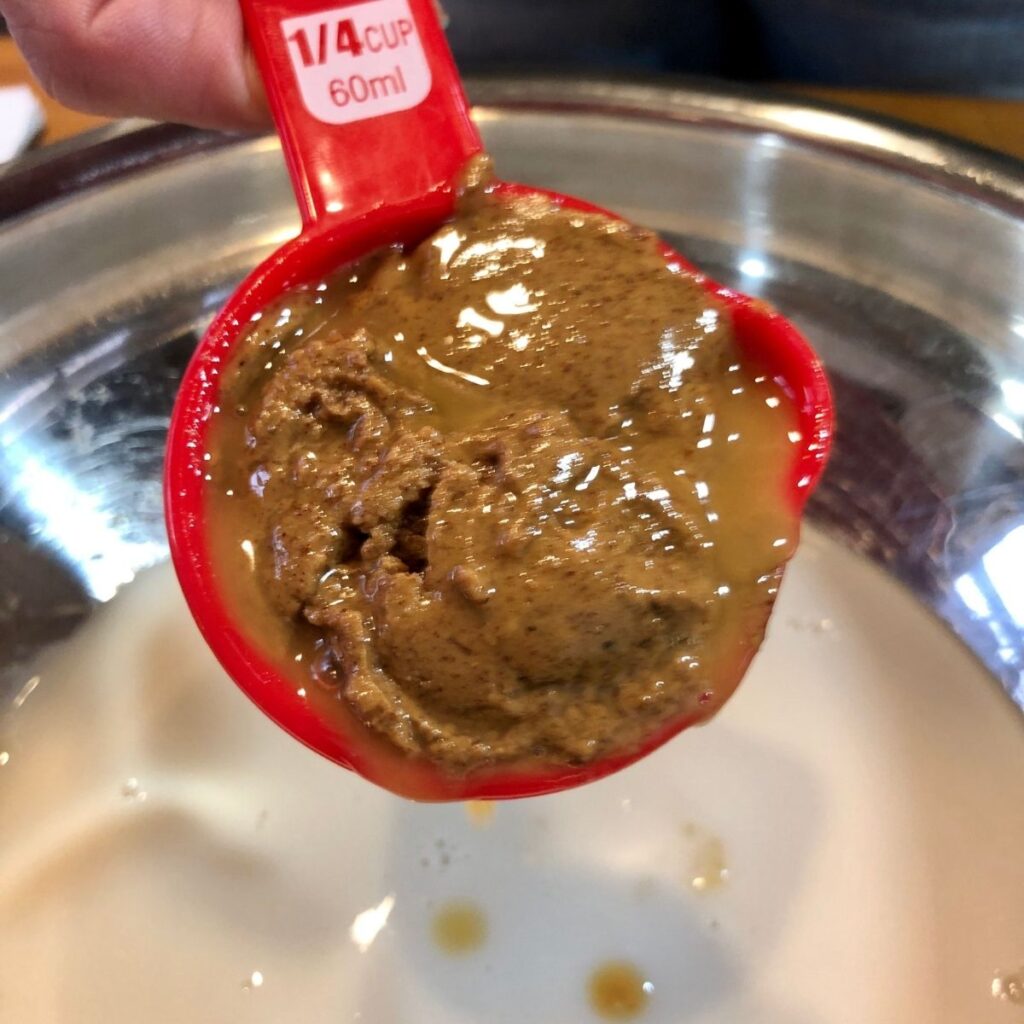 Almond butter in a red measuring cup over a bowl of almond milk in a stainless steel bowl