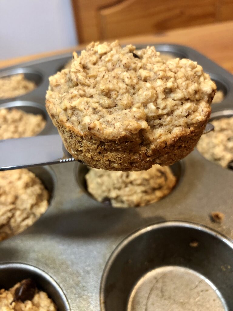 WW Banana Chocolate Chip Muffin on a spatula ver a muffin tin filled with WW breakfast muffins