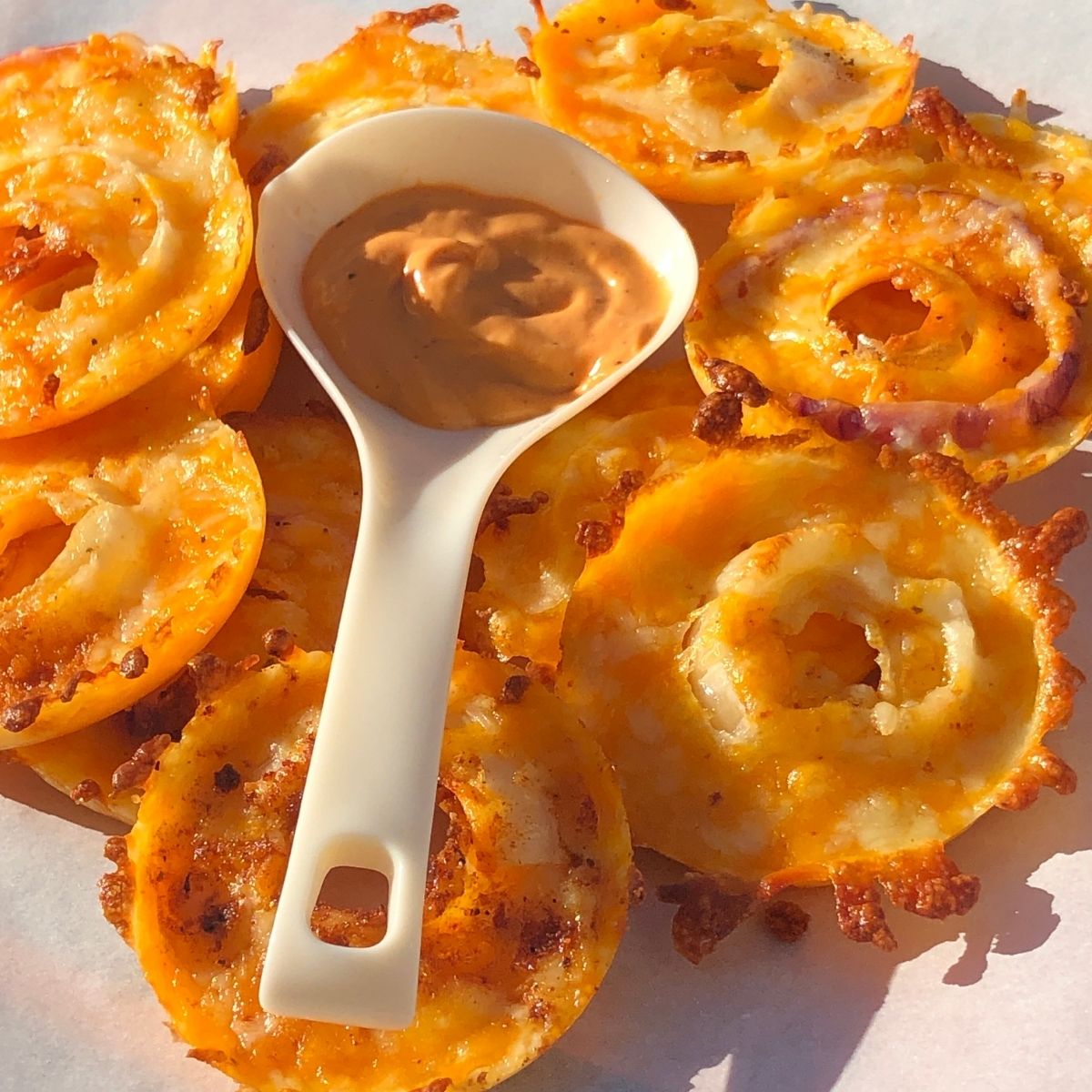 Cheesy Keto Onions Rings on a Parchment Paper with a white spoon holding spicy mayo