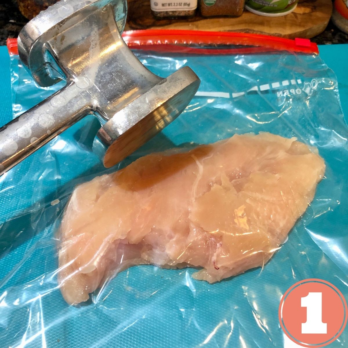A boneless skinless chicken breast in a Zip Loc bag with a meat tenderizer mallet