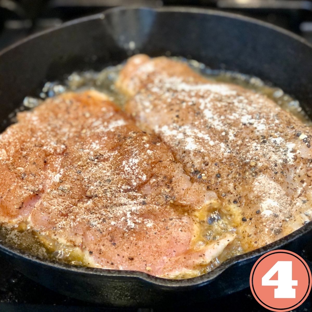 2 seasoned chicken cutlets cooking in a cast iron skillet