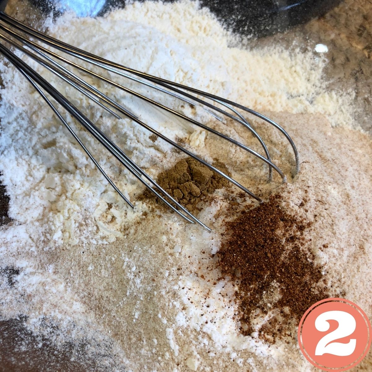 A whisk in a bowl with all purpose flour and whole wheat flour and cinnamon and nutmeg