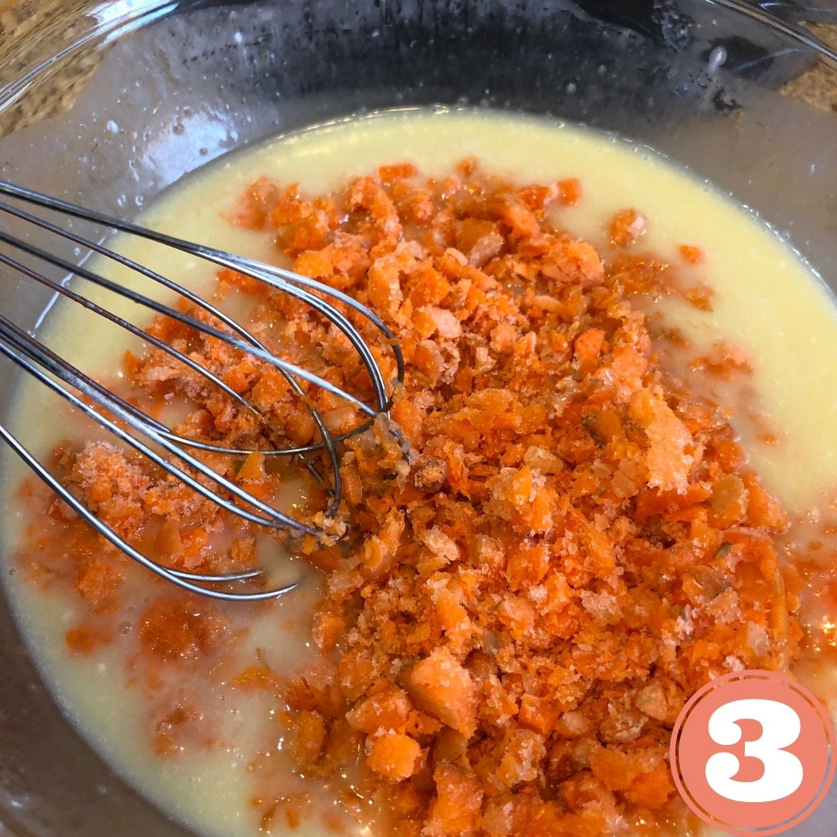 Grated carrots and eggs and coconut milk in a stainless steel bowl with a whisk