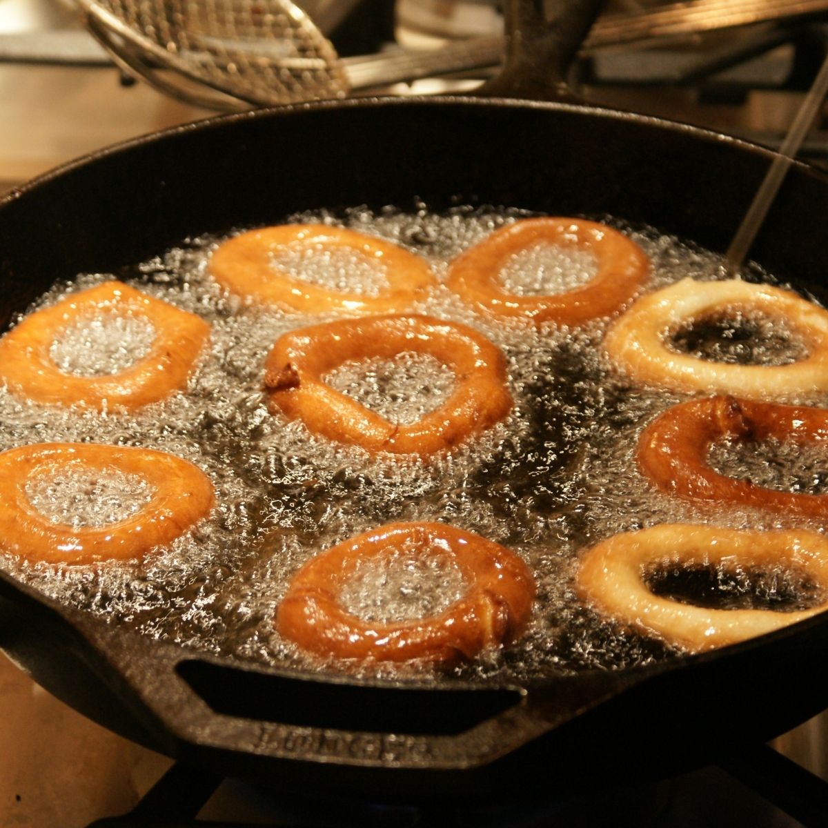 Onions rings frying in oil in a cast iron skillet