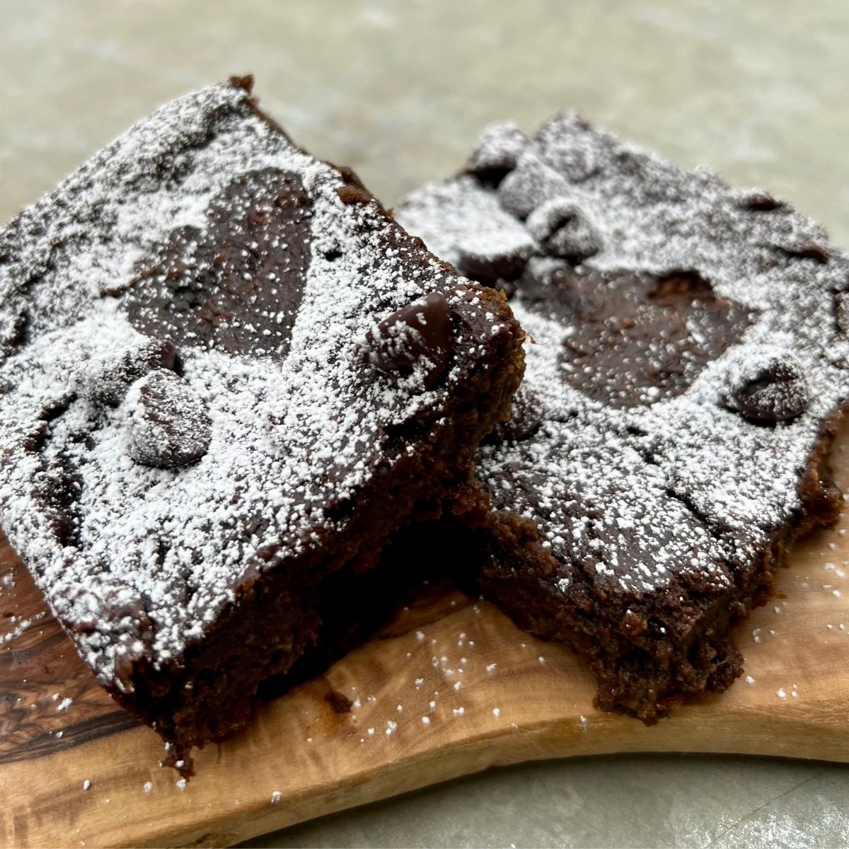 Two powdered sugar covered brownies on a piece of wood