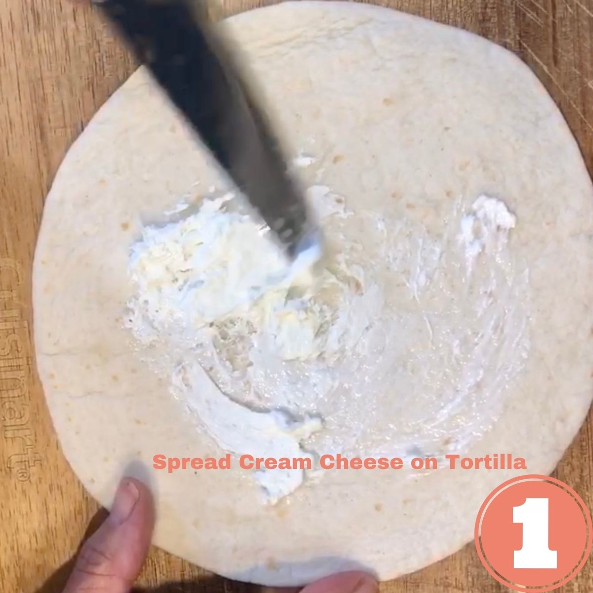 A butter knife spreading cream cheese on a tortilla