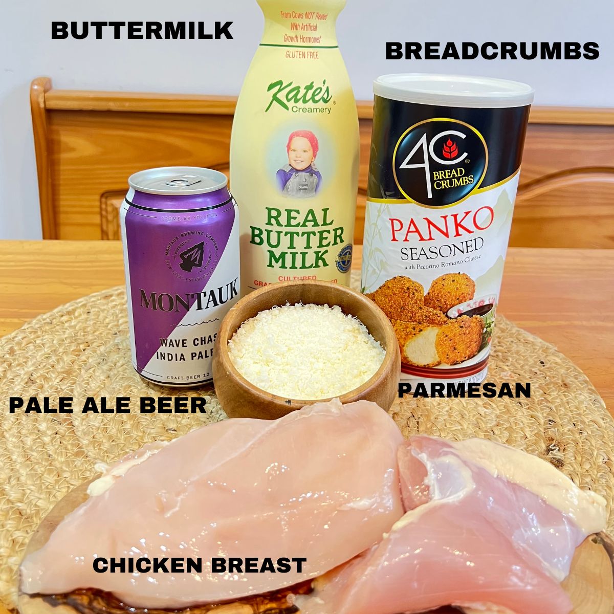 Chicken cutlets, a can of Montauk beer, a bottle of buttermilk, a can of Panko Breadcrumbs and parmesan cheese in a small wooden bowl on a table