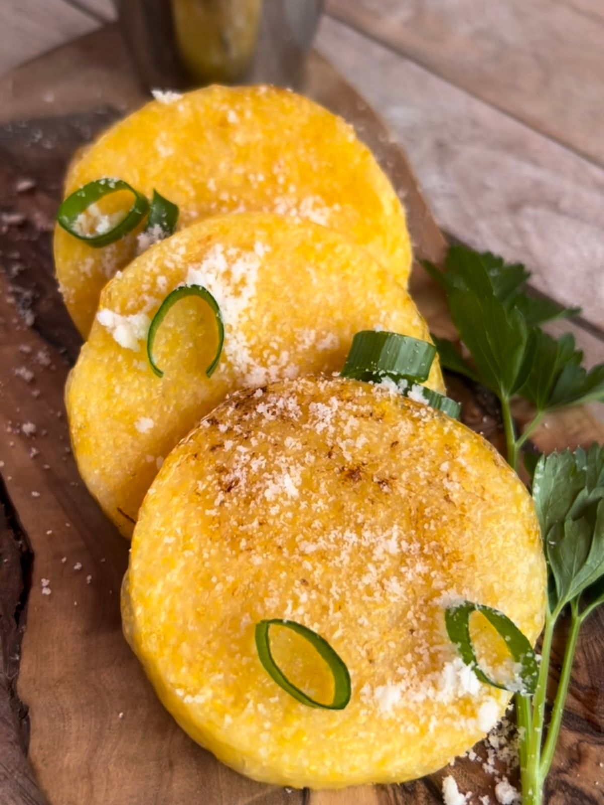 Baked polenta rounds on a cutting board with chopped chives