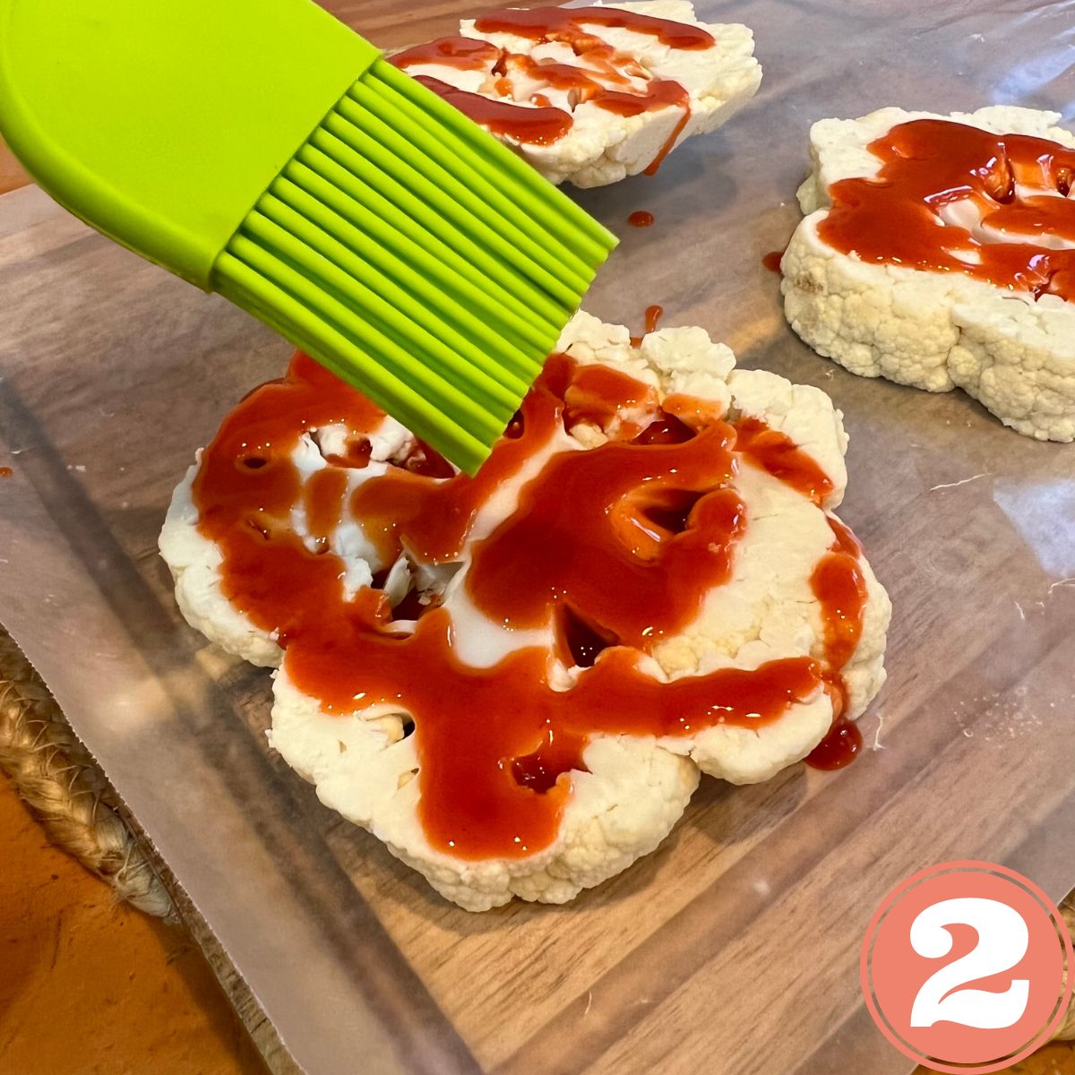 Cauliflower slices on a wooden cutting board brushed with hot sauce