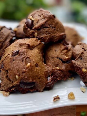 A pile of double chocolate chip cookies on a white plate with walnuts