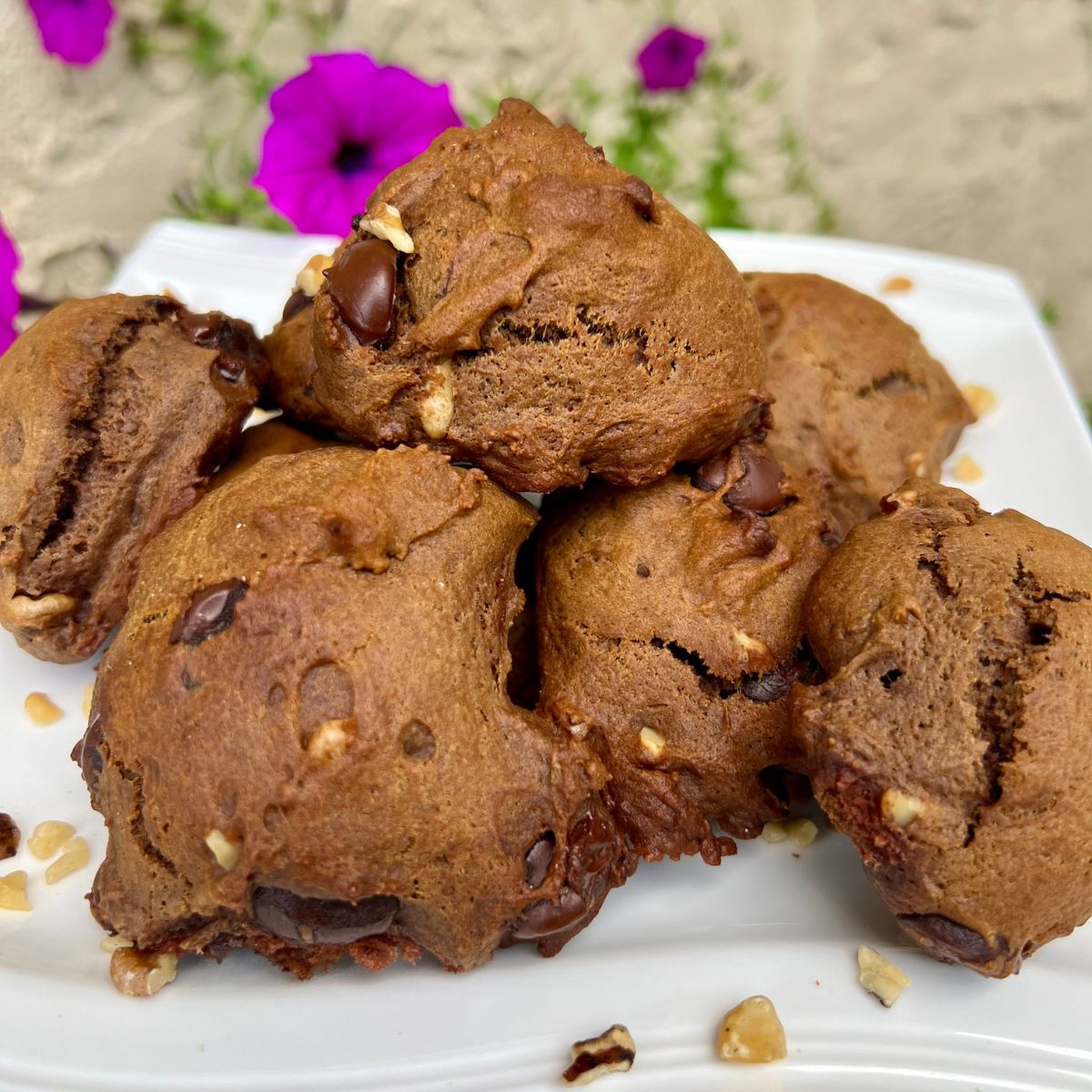 Double chocolate walnut cookies eggless on a white plate with a purple petunia