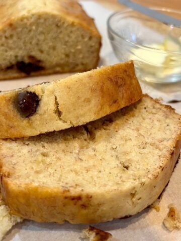 Slices of chocolate chip banana bread on parchment paper with a small glass bowl filled with butter