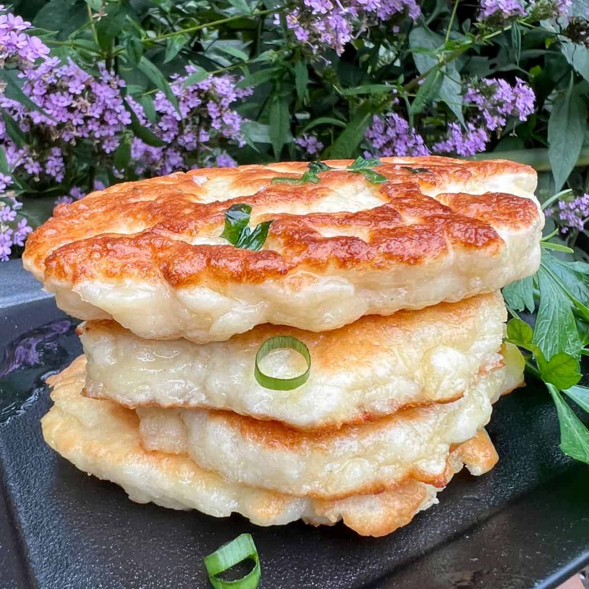 Homemade Naan Bread slices stacked on a black plate in a garden with purple flowers