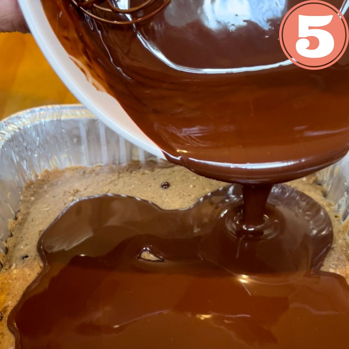 Melted chocolate being poured over cookie dough in a pan