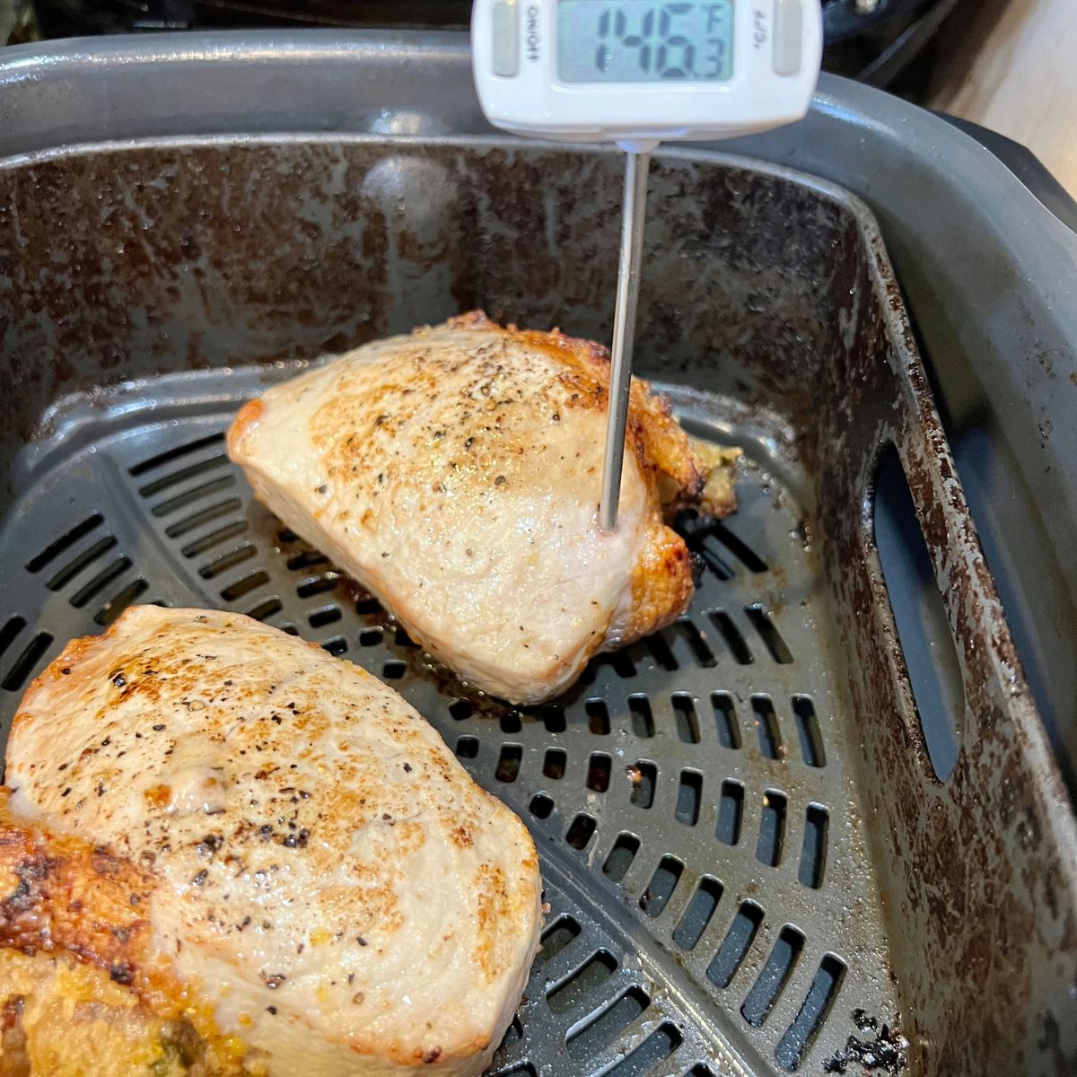 two stuffed pork chops in an air fryer basket with a meat thermometer inserted