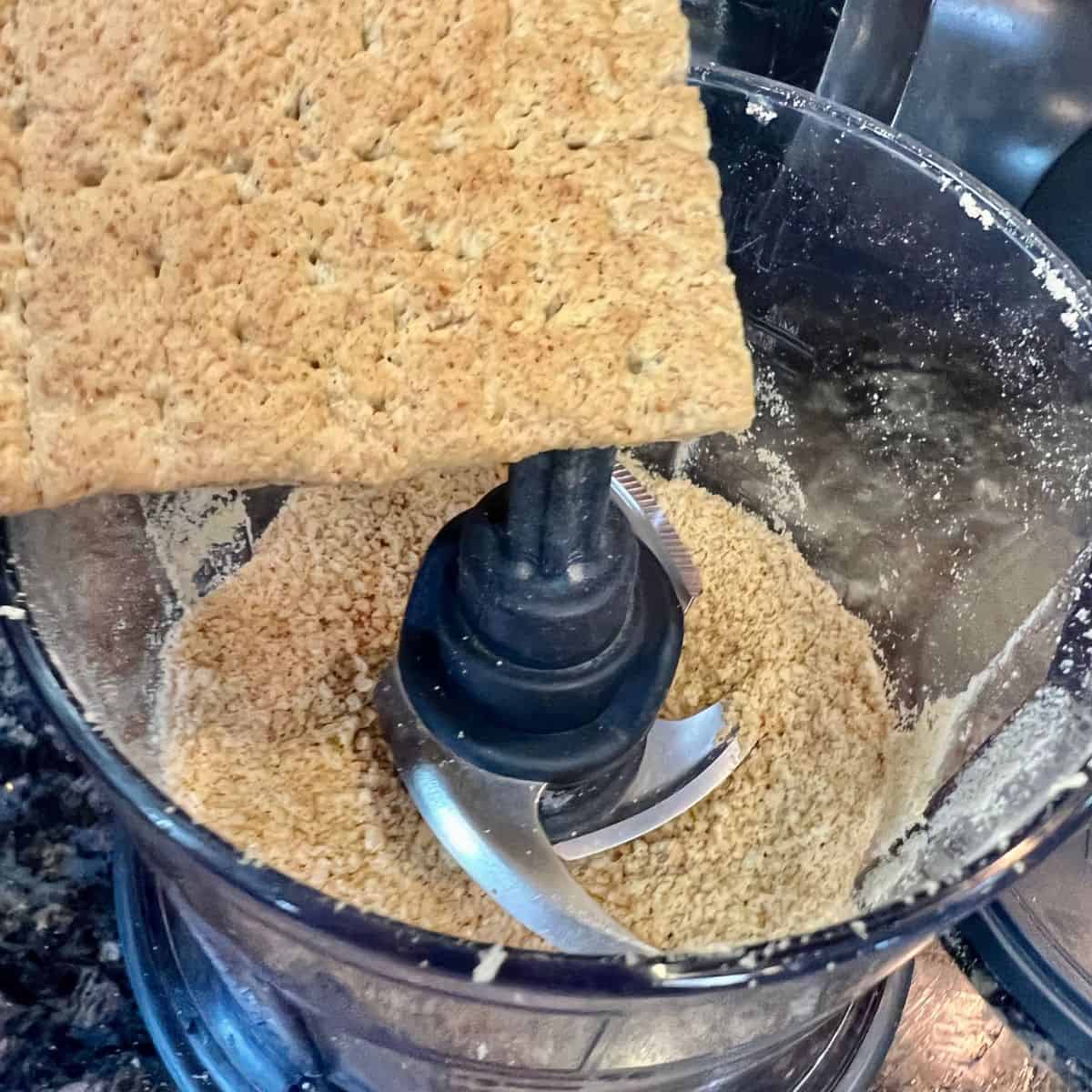 a graham cracker being placed in a mini ninja food processor