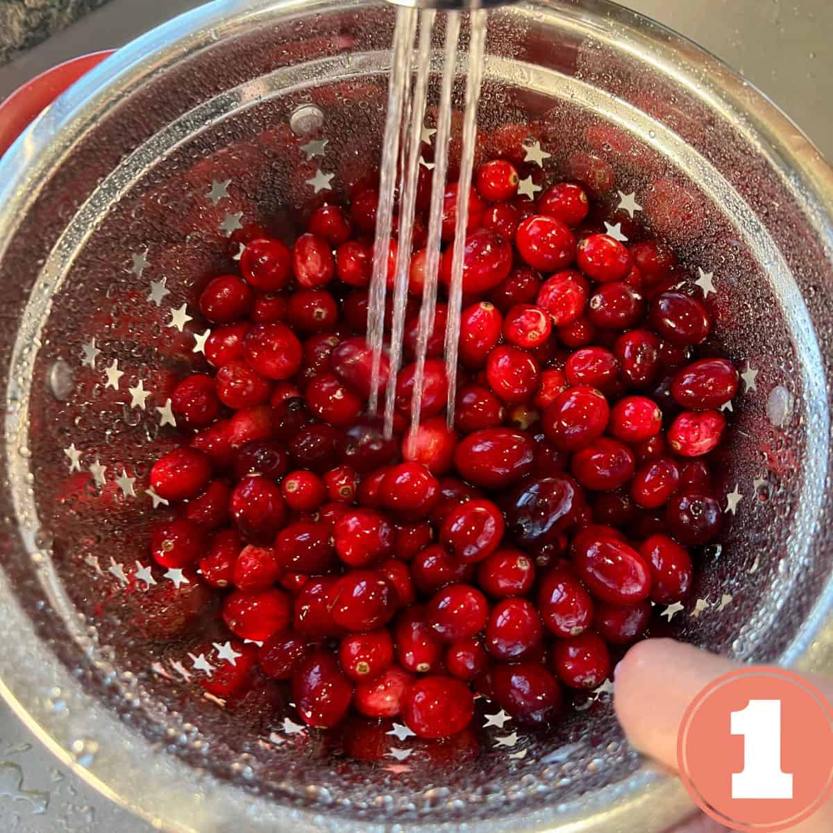 Rinsing fresh cranberries under a sink faucet in a stainless steel colander