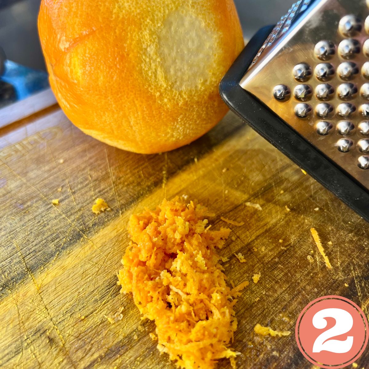 An orange being zested on a cutting board with a pile of orange zest