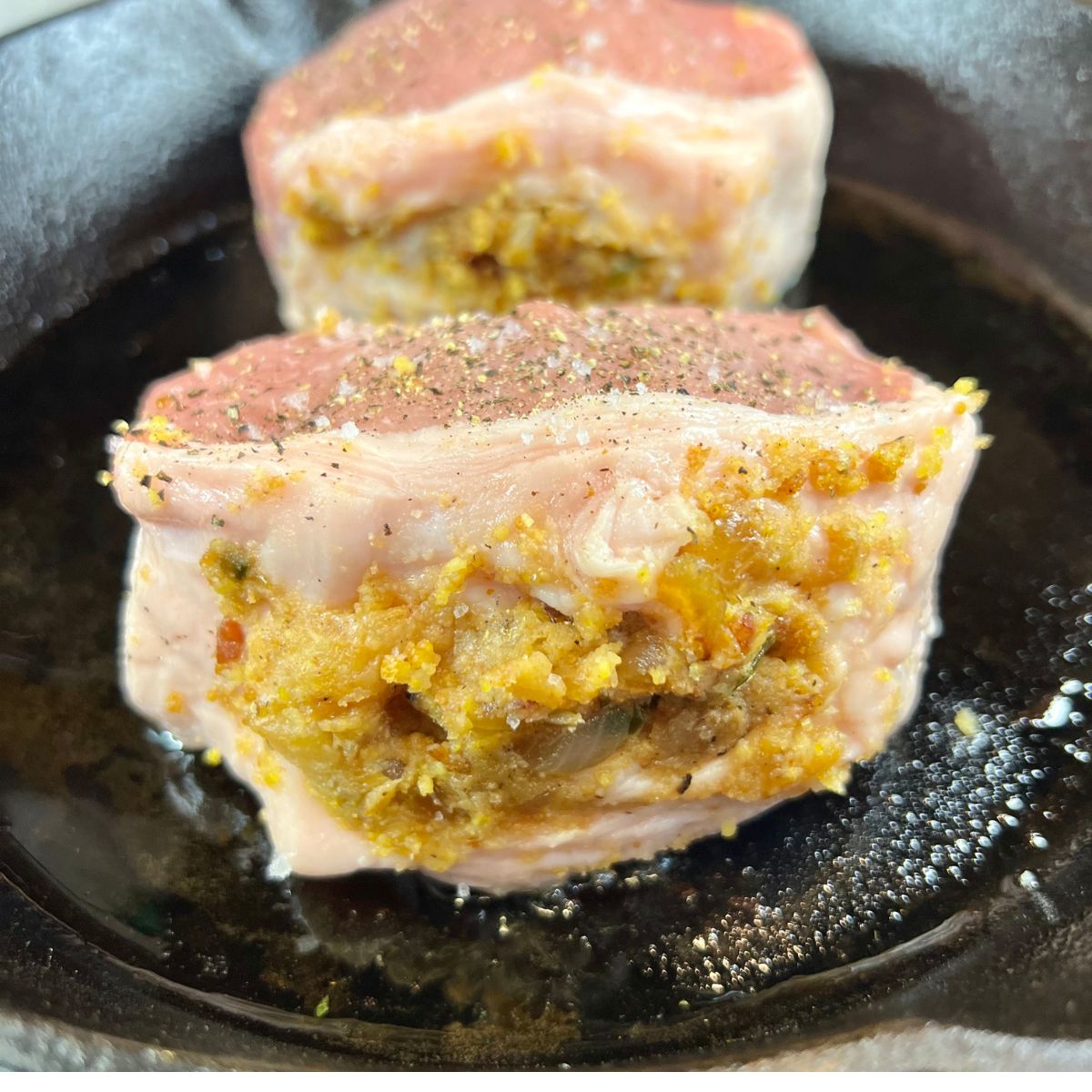 2 stuffed pork chops being seared in a cast iron skillet