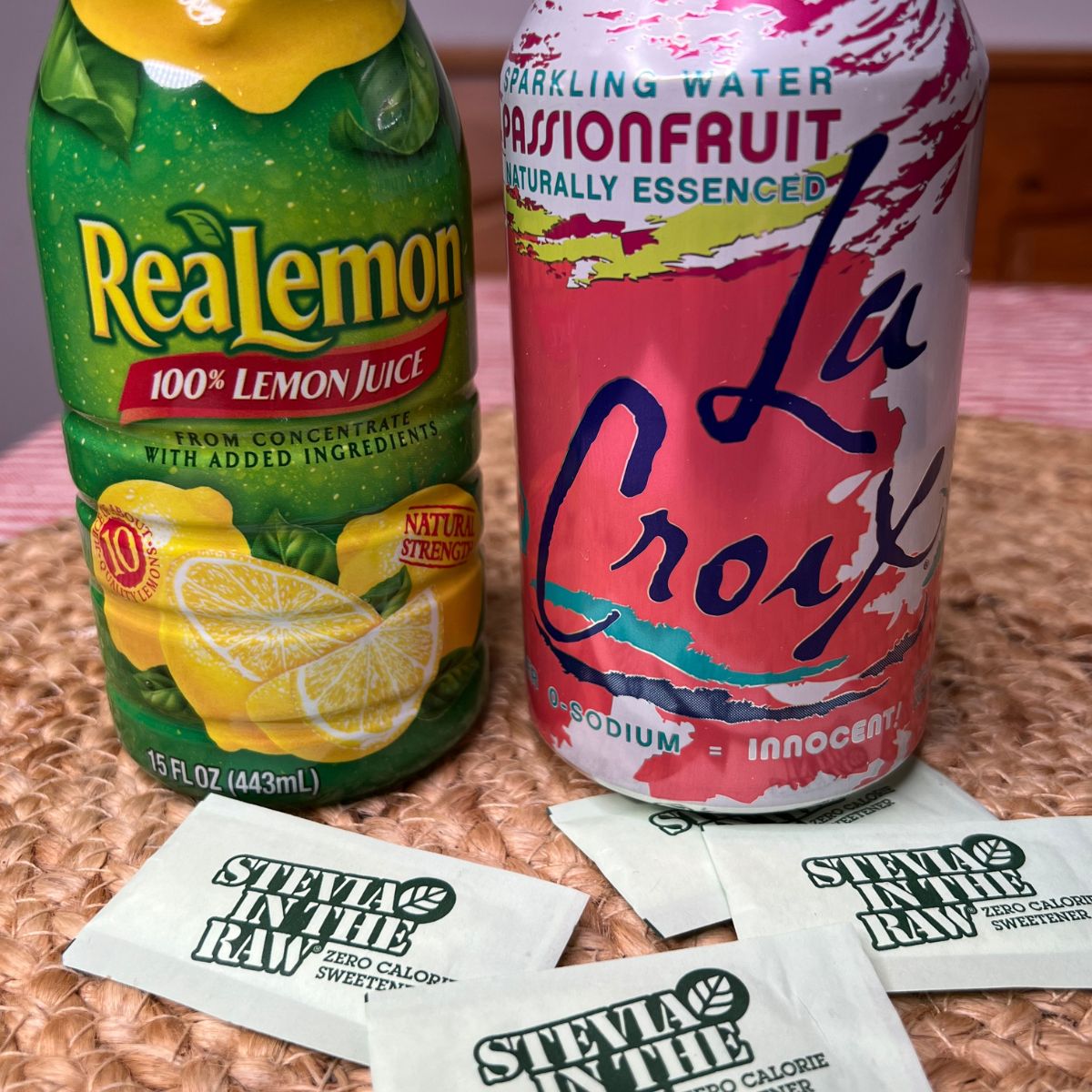 A bottle of lemon juice, a can of La Croix Passion Fruit Sparkling water and 3 packets of Stevia on a table