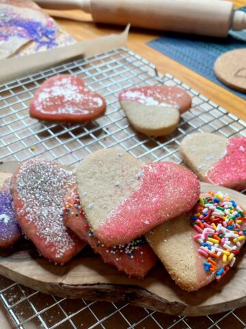 2 Ingredient Heart shaped cookies stacked on a wooden board with a rolling pin and cooking baking tray