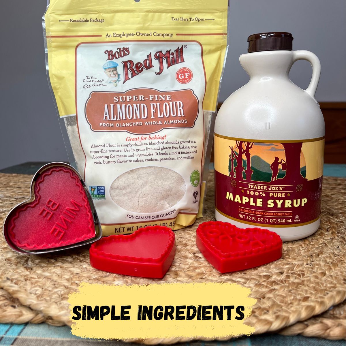 A bag of almond flour and a jug of maple syrup and heart shaped cookie cutters