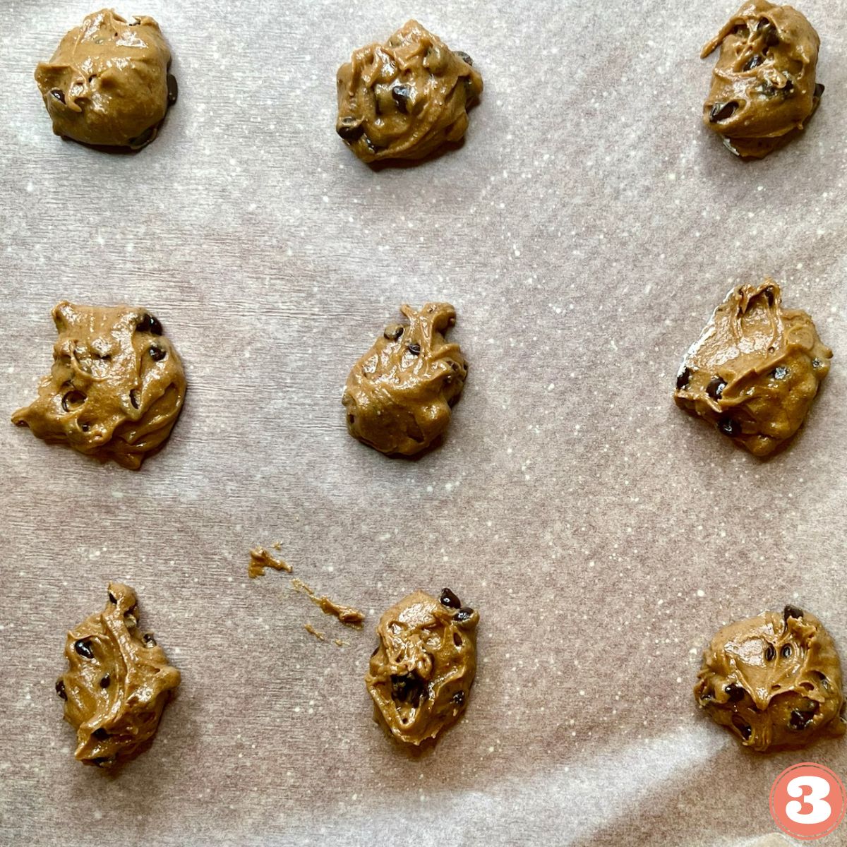 Chocolate Chip Cookie dough dollops on a baking pan lined with parchment paper