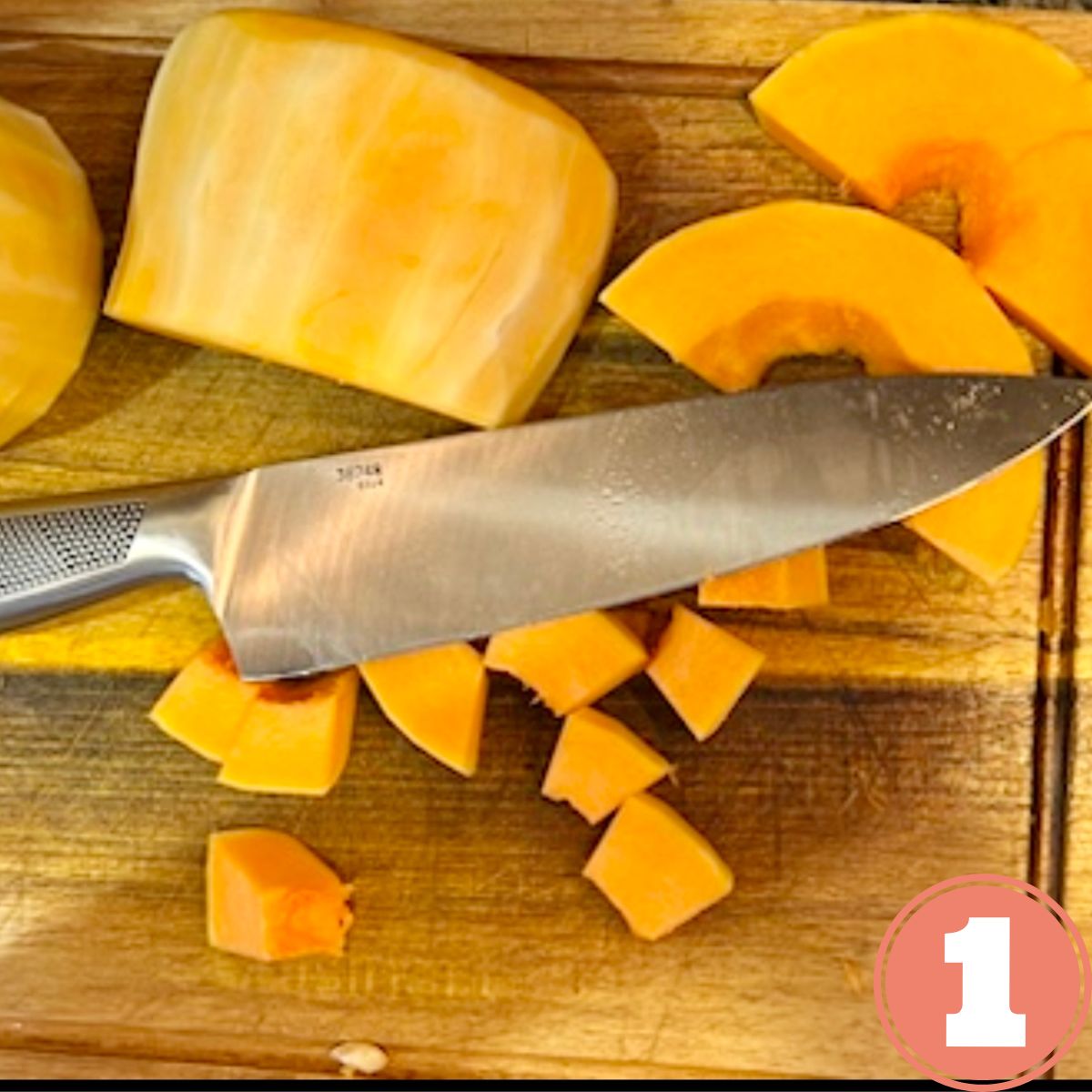 Cubed butternut squash on a wooden cutting board with a large stainless steel knife