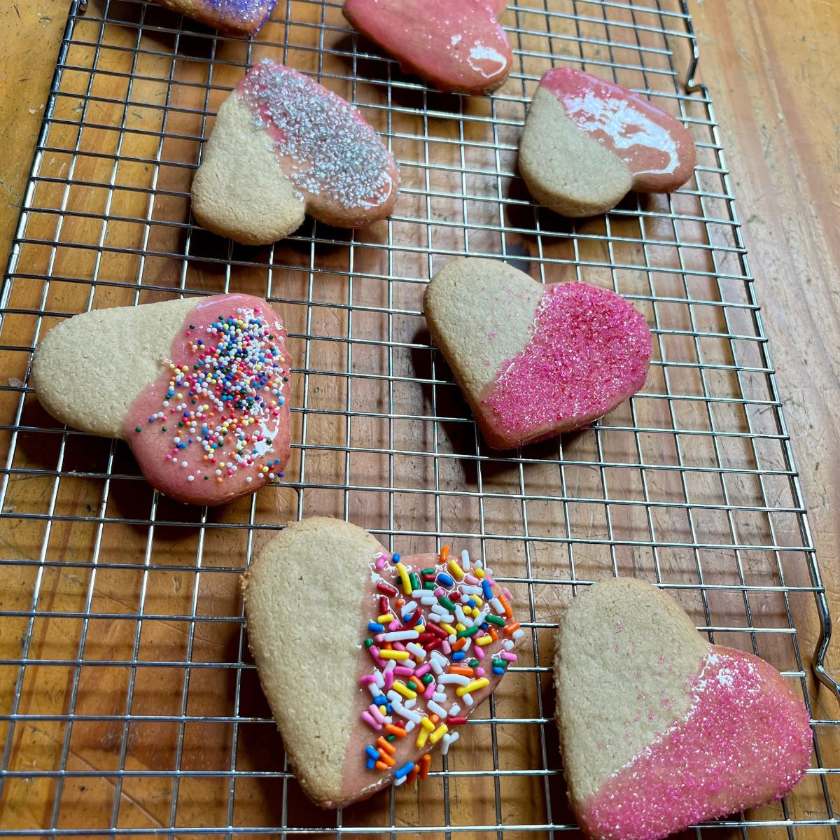 Iced and sprinkle dipped heart shaped two ingredient sugar cookies on a rack