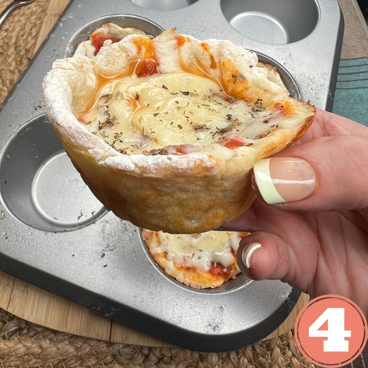 One individual deep dish pizza being held in a hand over a muffin tin