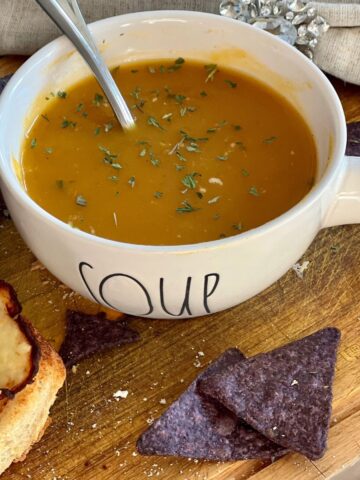 Zero Point Butternut Squash Soup in a white bowl on a wooden table with blue chips