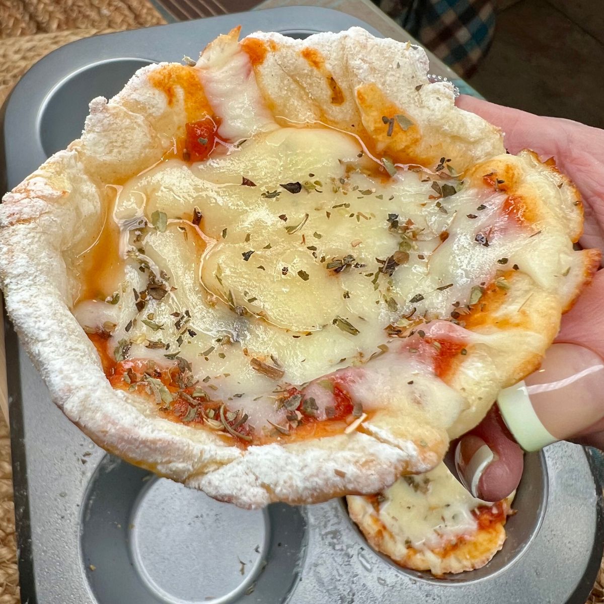A hand holding a mini deep dish pizza over a muffin tin