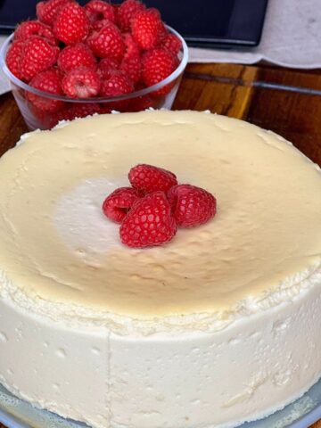 Easy crustless vanilla cheesecake with raspberries on top sitting on a wooden table next to a bowl of raspberries