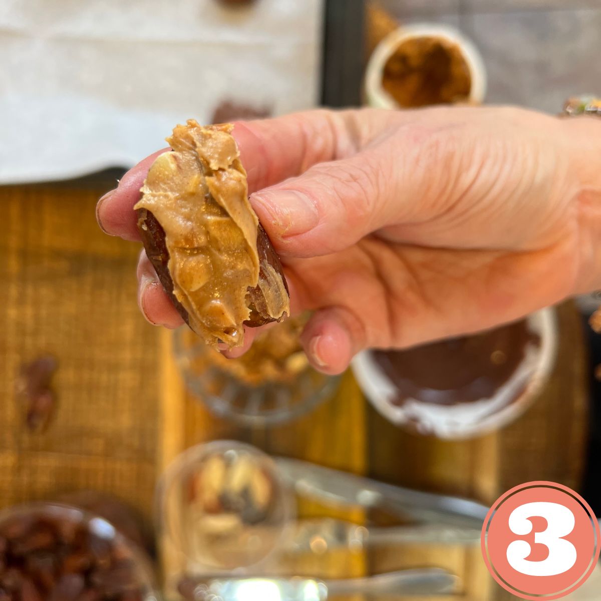 A hand holding a homemade snickers bar made with dates covered in nut butter