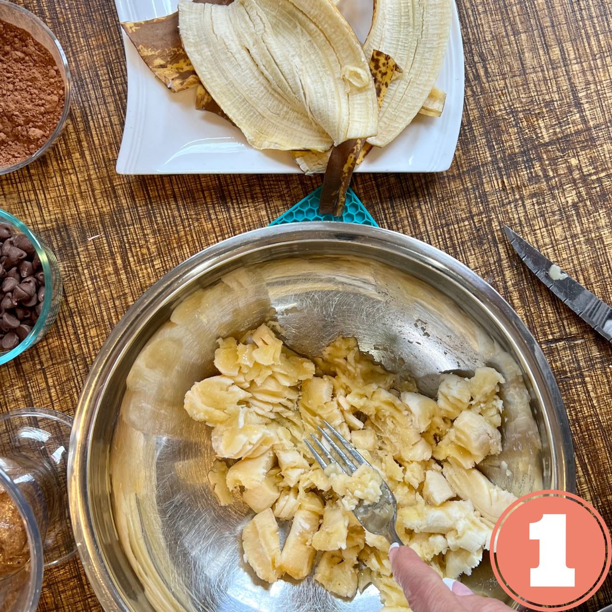 Mashing bananas with a fork in a stainless steel bowl