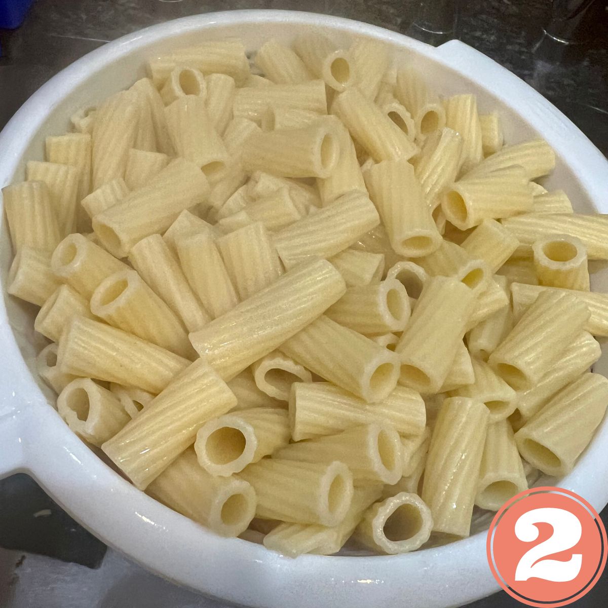 Ziti pasta being strained in a white colander