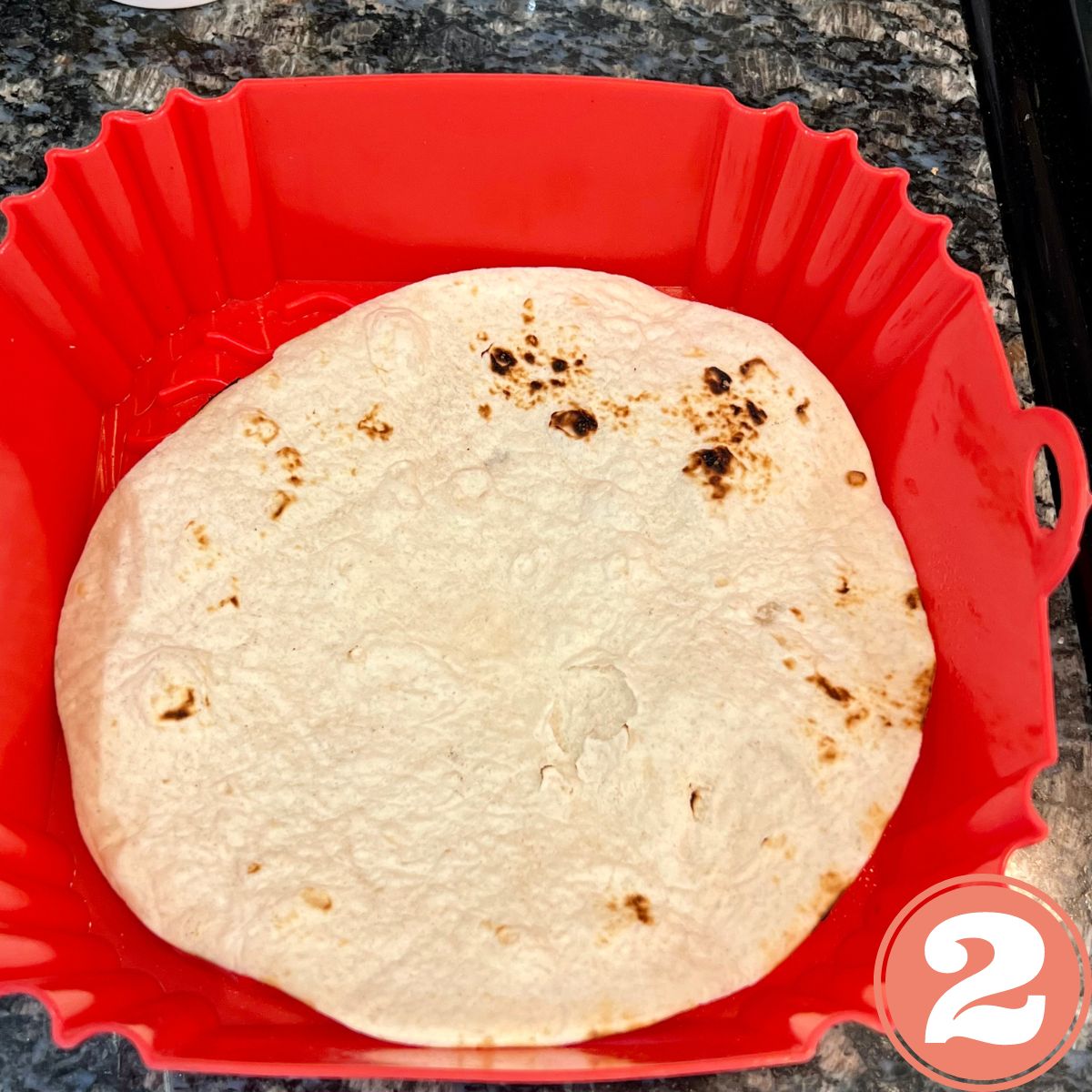 A flour tortilla in a red silicone air fryer liner