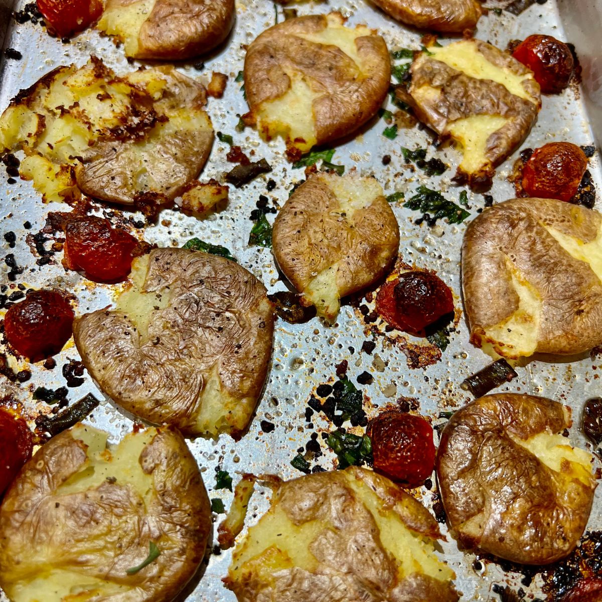 Air fryer smashed potatoes on a baking sheet pan with cherry tomatoes and herbs